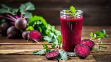 A glass of beet juice garnished with a green leaf sits on a wooden table, surrounded by whole beets, sliced beets, and beet leaves—highlighting the health perks and irresistible beetroot juice benefits.